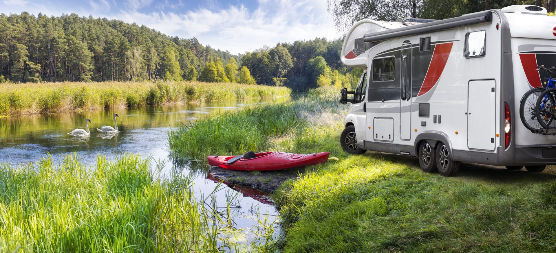 RV parked beside lush, green riverbank