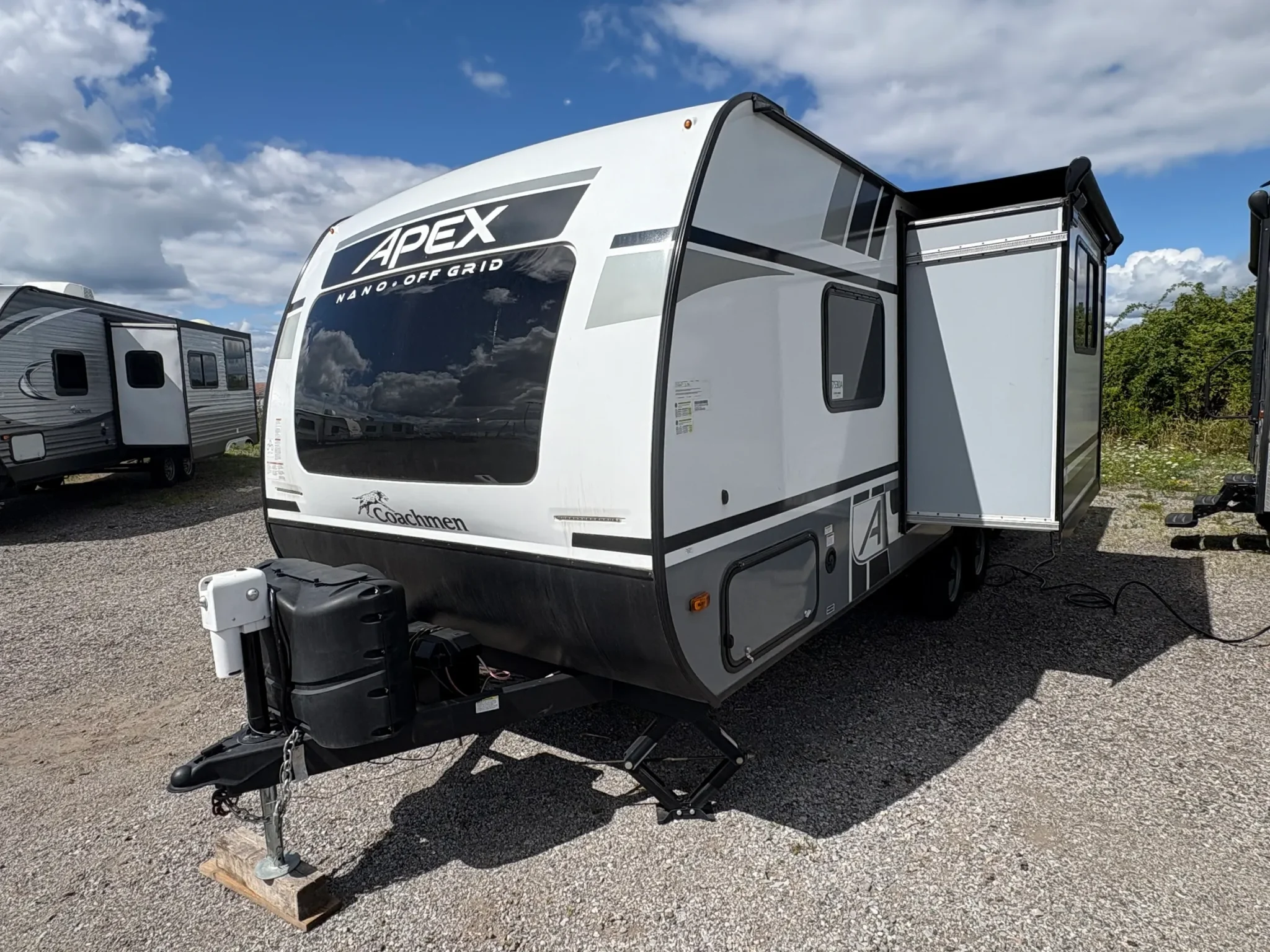 Modern travel trailer parked on gravel lot.